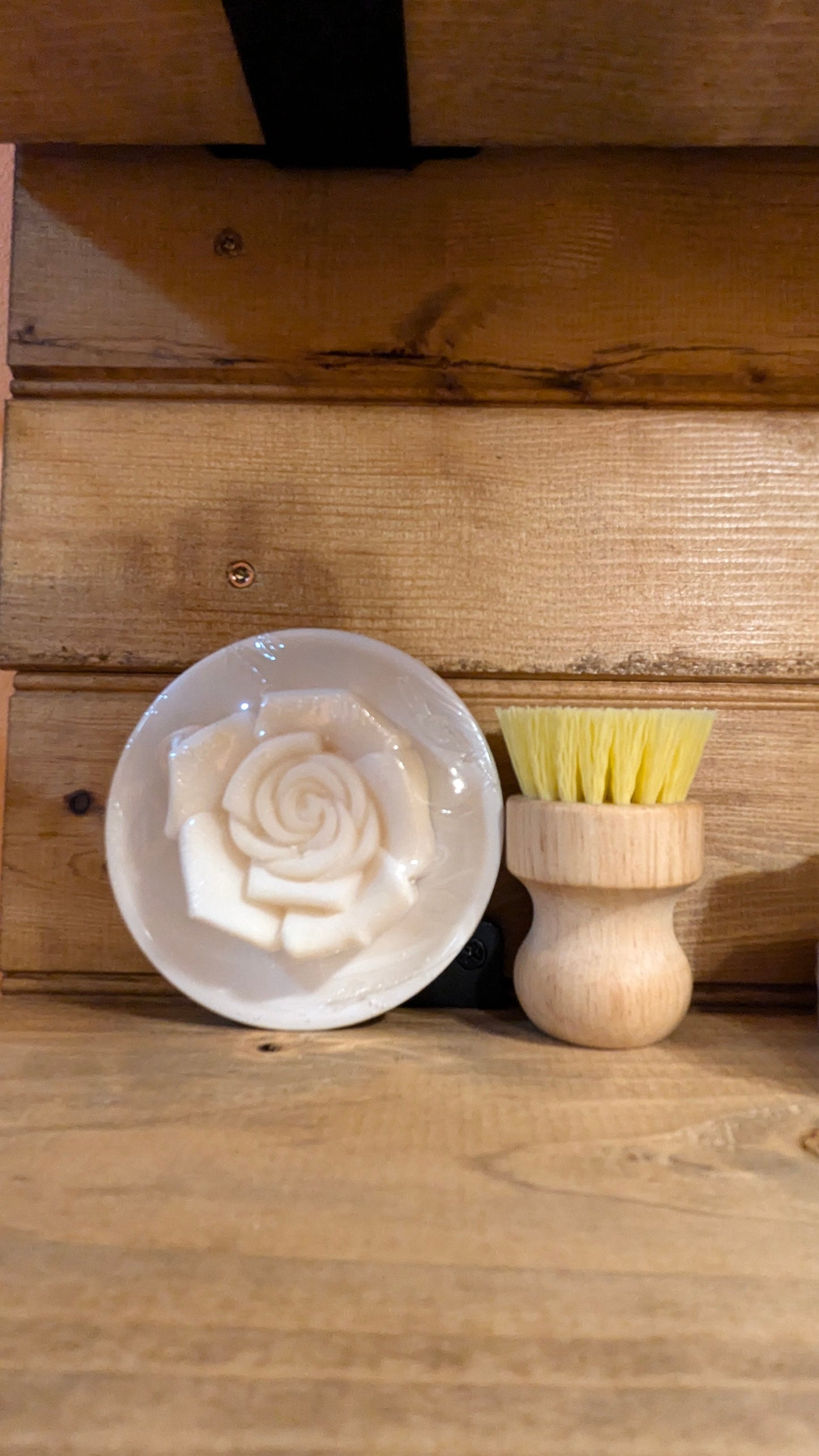 White soap with a floral design on a wooden surface next to a shaving brush seen @ CarolinaCart.com
